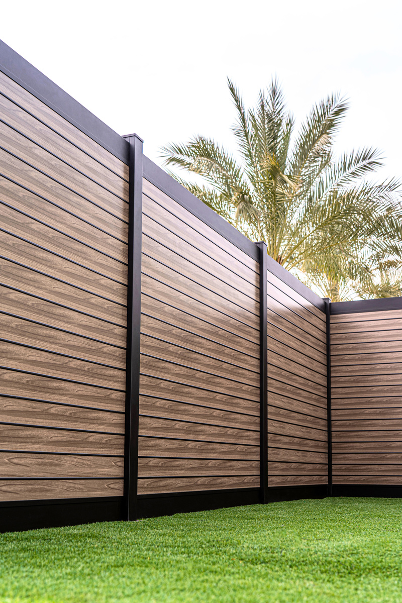 Modern aluminum fence with wood-like texture against a green lawn and palm trees, offering a stylish and maintenance-free fencing solution.