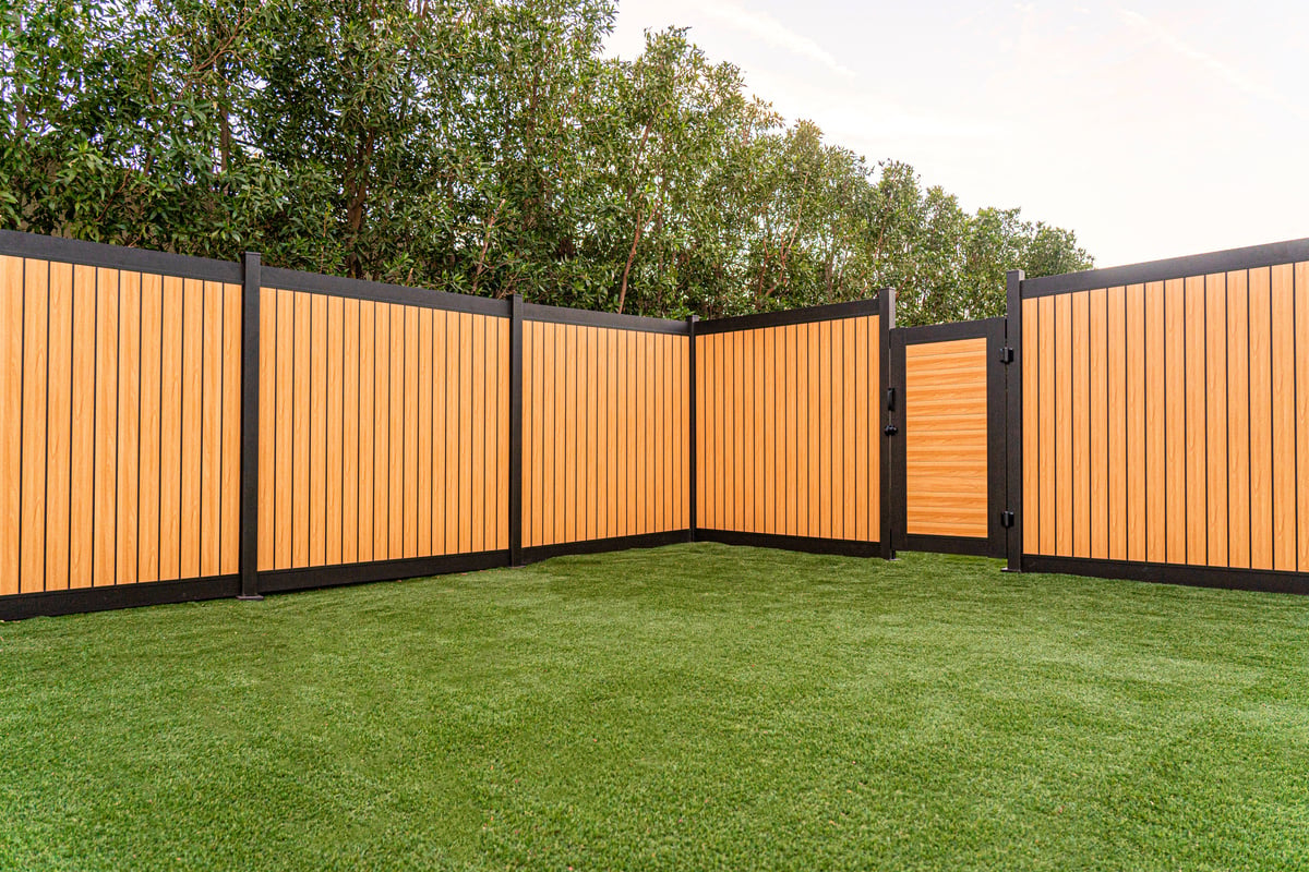 Aluminum fence with a natural wood-like finish, featuring a matching gate, set against a backdrop of lush greenery