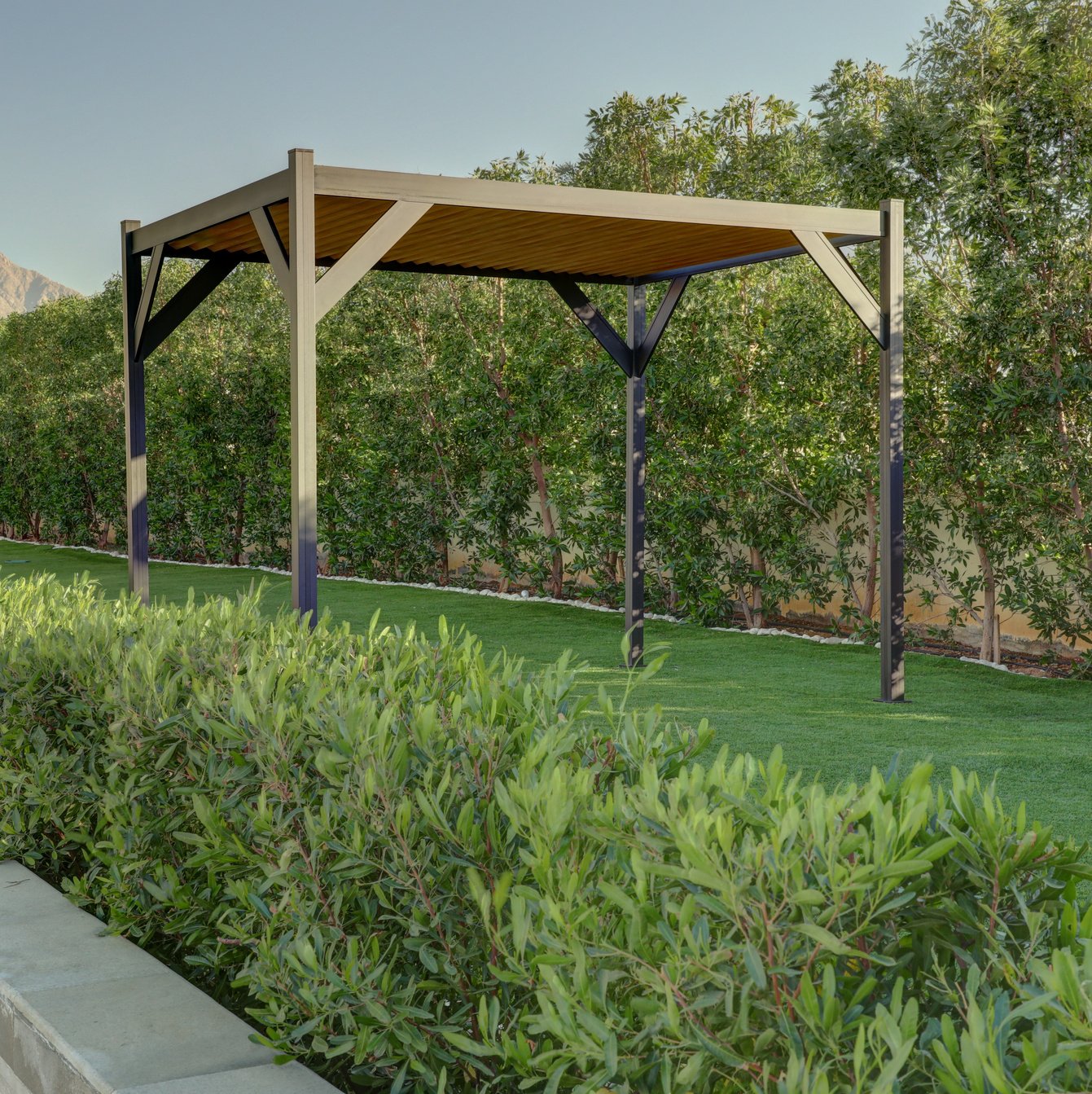 Modern aluminum pergola with a wood-like finish in a lush garden setting, offering shade and style for outdoor spaces.