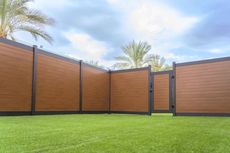 Modern aluminum fence with a wood-like finish, set against a lush lawn and palm trees, offering a stylish and durable fencing solution for residential properties.